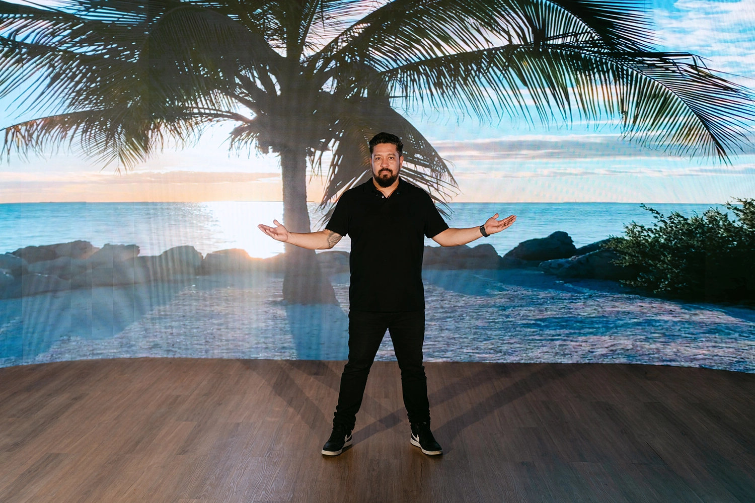 Elisio Neto diante do painel de LED exibindo uma praia com coqueiros
